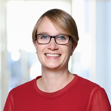 Luisa Gebhardt hat kurze blonde Haare. Sie trägt eine Brille und ein rotes Oberteil.