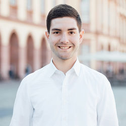 Niklas Sabel hat kurze braune Haare. Er trägt ein weißes Hemd und steht vor dem Mannheimer Schloss.