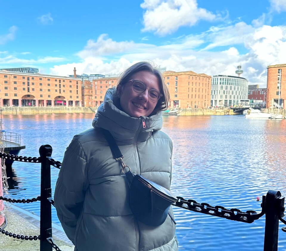 Miriam Gemming in dicker Jacke auf einer Brücke mit AUsblick auf Fluss und Gebäude.