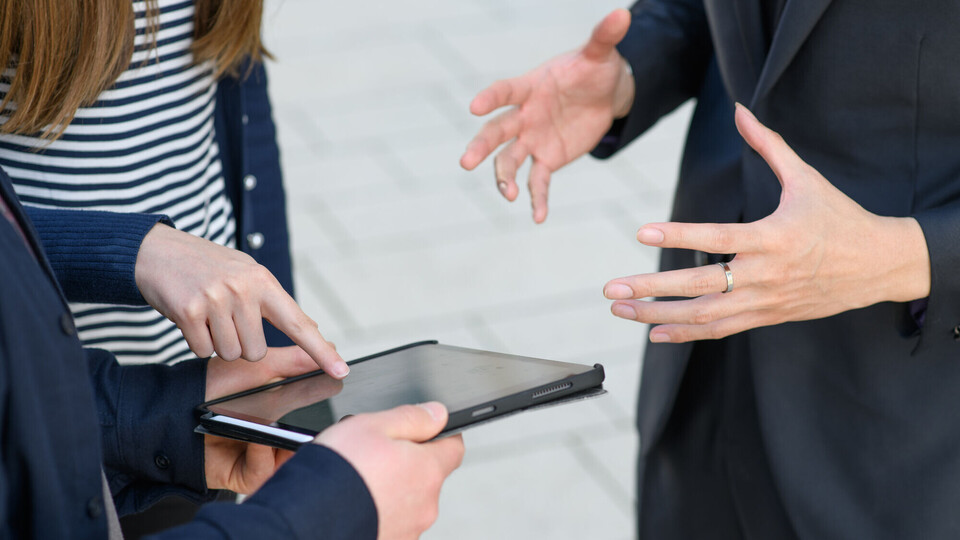 Drei Personen stehen um ein Tablet und gestikulieren mit den Händen. 