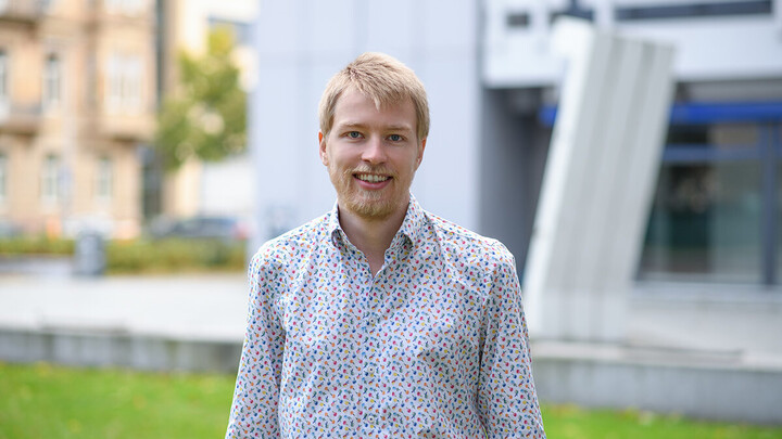 Felix Jäger. He is wearing a black-dotted shirt and is standing in front of the A5 building.