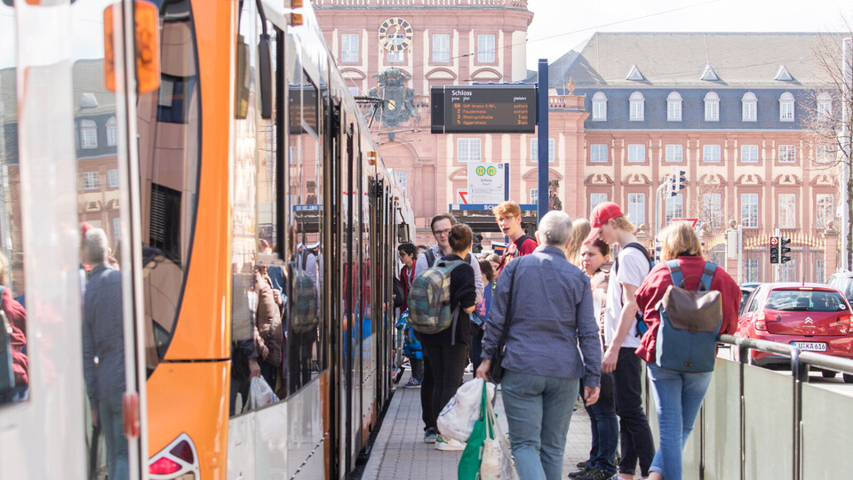 Menschen steigen an einer Straßenbahnhaltestelle vor dem Mannheimer Schloss ein und aus.
