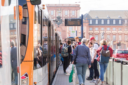 Menschen steigen an einer Straßenbahnhaltestelle vor dem Mannheimer Schloss ein und aus.