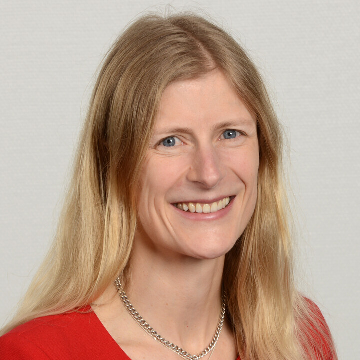 Liz Ascherl mit langen blonden Haaren und einem roten Blazer offen lächelnd