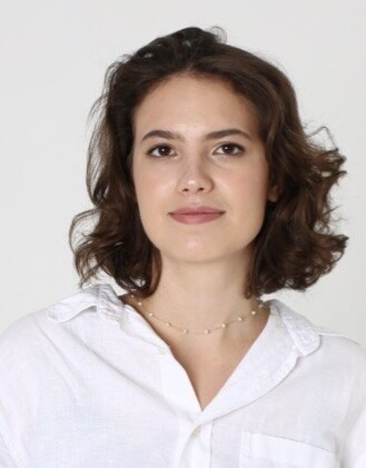 Portrait von Kateryna Butyrina. Sie trägt eine weiße Bluse und steht vor einer weißen Wand.