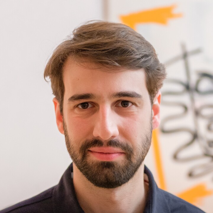 Eine Person trägt ein dunkelblaues Hemd und steht vor einem weißen Hintergrund. Die Person heißt Cornelius Schneider.