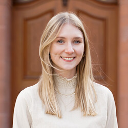 Marie Fox has long blond hair. She is wearing a light-colored turtleneck sweater.