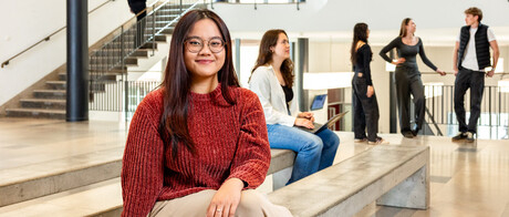 Eine Studentin sitzt auf einer Seitenbank im Ostflügel des Schlosses. Im Hintergund unterhalten sich weitere Studierende. 