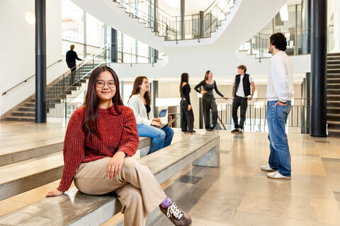 Eine Studentin sitzt auf einer Seitenbank im Ostflügel des Schlosses. Im Hintergund unterhalten sich weitere Studierende. 