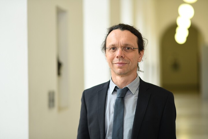 Portraitfoto von Prof. Dr. Dr. h.c. Dirk Ifenthaler in einem Gang im Schloss Mannheim. Er trägt ein graues Hemd, eine schwarz-grau gemusterte Krawatte und ein schwarzes Sakko.