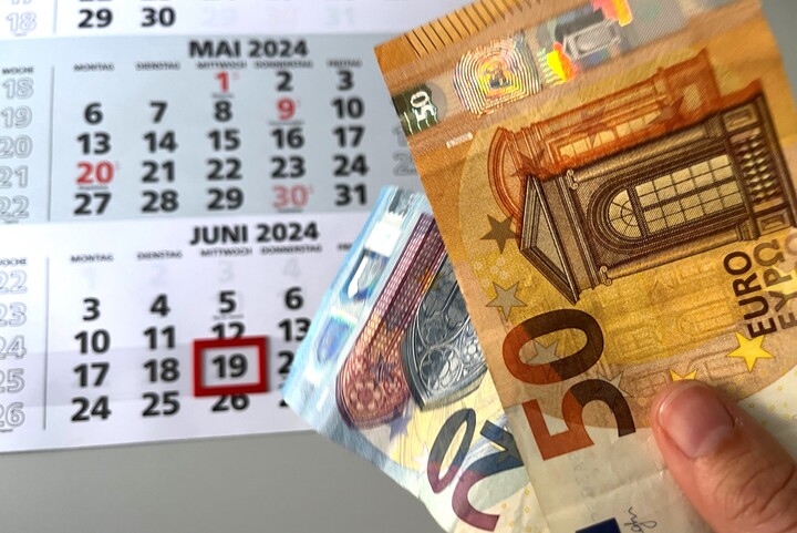 The background shows a calendar with a day circled in red. In the foreground there is a hand holding a 50 euro bill and a 20 euro bill.