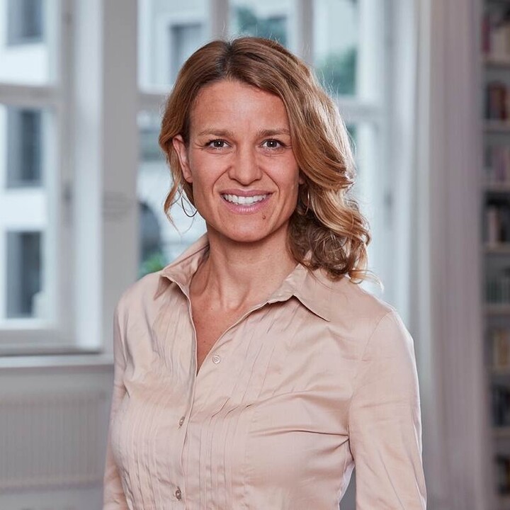 Eine lächelnde Person trägt eine altrosa-farbene Bluse und steht vor einem Fenster. Die Person heißt Nadine Klass.