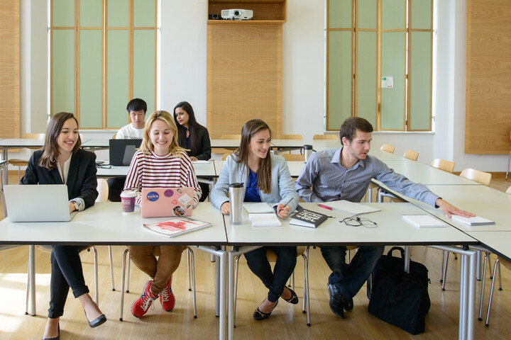 Sechs Studierende arbeiten in einem Seminarraum. Vor ihnen liegen Laptops, Notizblöcke und Bücher.