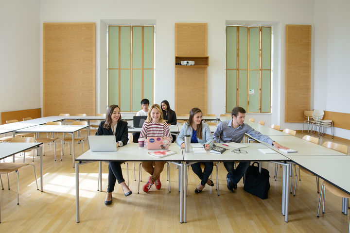 Sechs Studierende arbeiten in einem Seminarraum. Vor ihnen liegen Laptops, Notizblöcke und Bücher.
