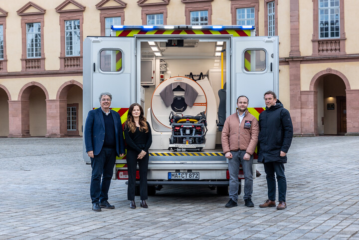 Vier Personen stehen vor dem spezialisierten Rettungswagen auf dem Ehrenhof. Im Inneren ist das mobile CT zu sehen.