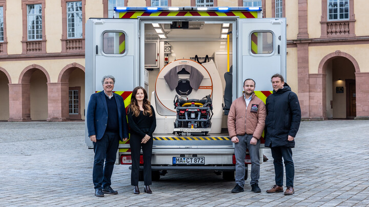 Vier Personen stehen vor dem spezialisierten Rettungswagen auf dem Ehrenhof. Im Inneren ist das mobile CT zu sehen.