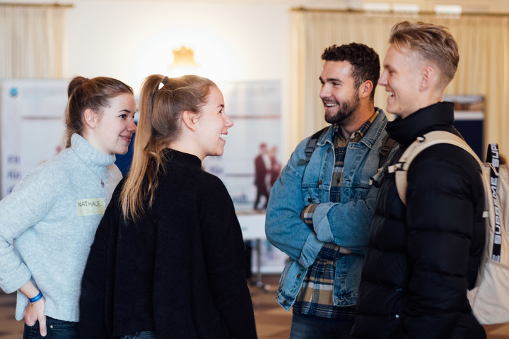 Zwei Studentinnen und zwei Studenten stehen sich gegenüber, unterhalten sich und lachen