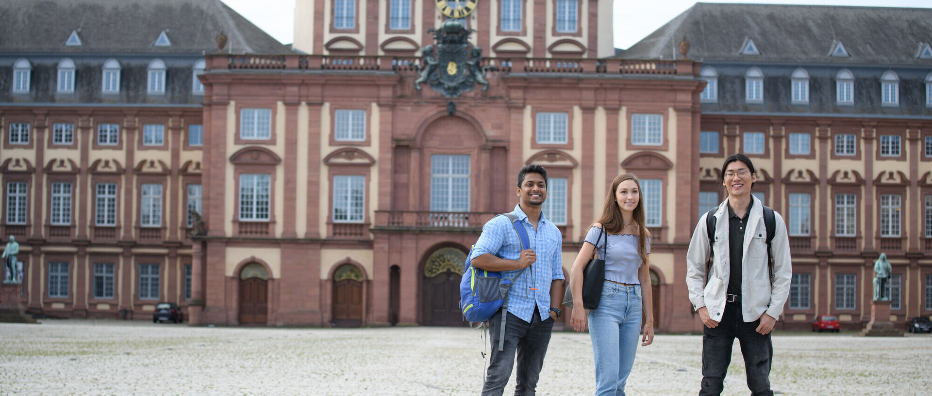Three students in the castle courtyard look towards the camera. The central building of the palace in the background.