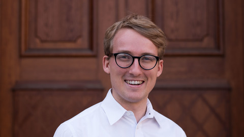 Gerrit von Zedlitz. He is wearing a white shirt and is standing in front of one of the castle doors.