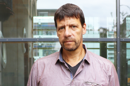 Porträt von Professor Krause, der vor einer Glaswand steht, ein lilafarbenes Hemd trägt und in die Kamera schaut.
