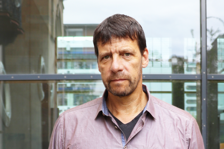 Porträt von Professor Krause, der vor einer Glaswand steht, ein lilafarbenes Hemd trägt und in die Kamera schaut.