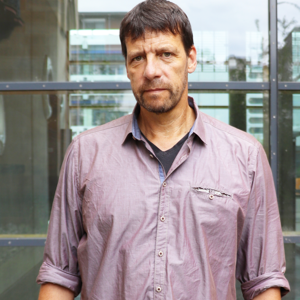 Porträt von Professor Krause, der vor einer Glaswand steht, ein lilafarbenes Hemd trägt und in die Kamera schaut.