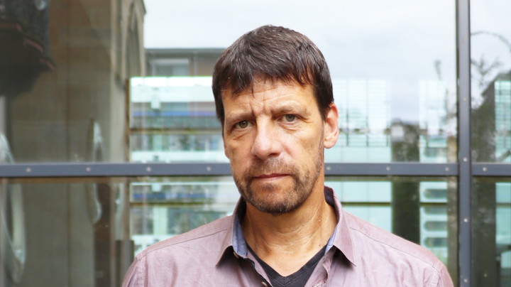 Porträt von Professor Krause, der vor einer Glaswand steht, ein lilafarbenes Hemd trägt und in die Kamera schaut.