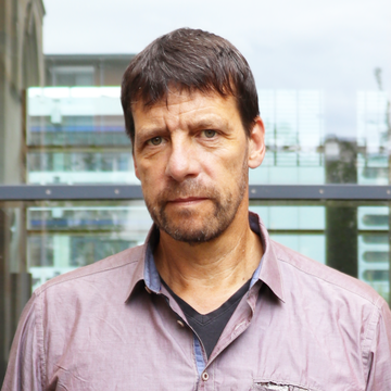 Porträt von Professor Krause, der vor einer Glaswand steht, ein lilafarbenes Hemd trägt und in die Kamera schaut.