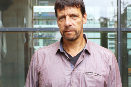Porträt von Professor Krause, der vor einer Glaswand steht, ein lilafarbenes Hemd trägt und in die Kamera schaut.