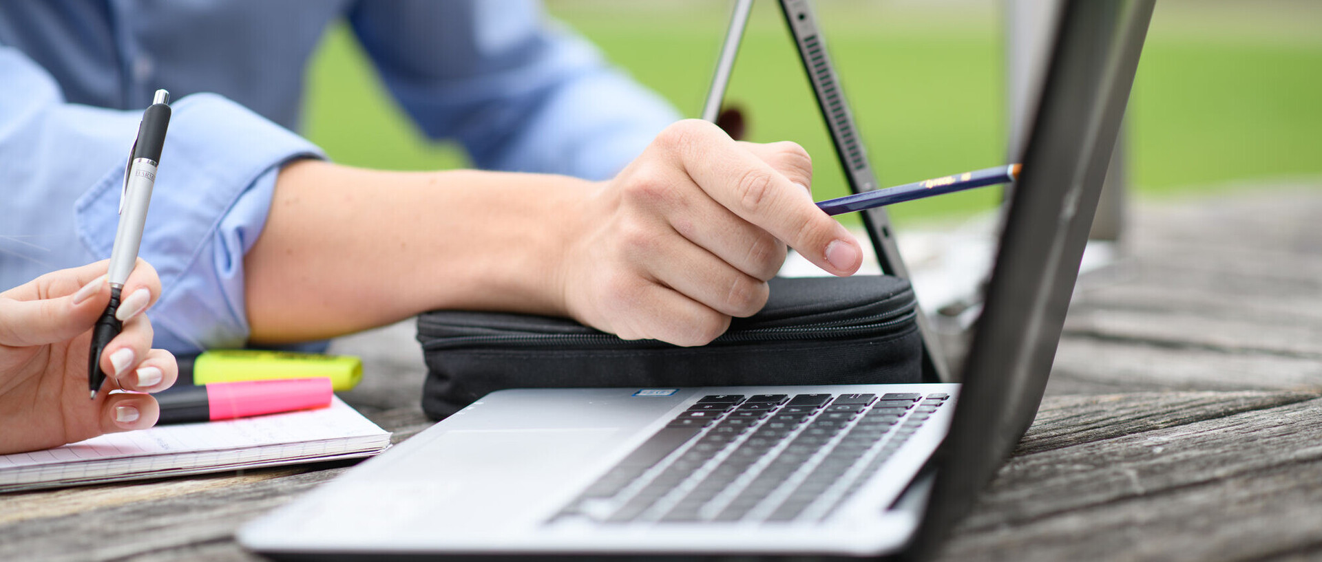Ein Laptop steht auf einem Tisch im Freien. Eine Person zeigt mit einem Stift auf den Bildschirm des Laptops.