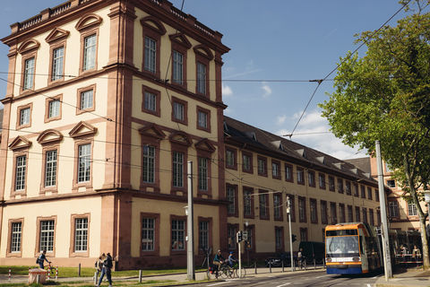 Der Eckturm am Ostflügel des fensterreichen Mannheimer Schlosses. Auf der Straße fahren eine Straßenbahn und Radfahrer.