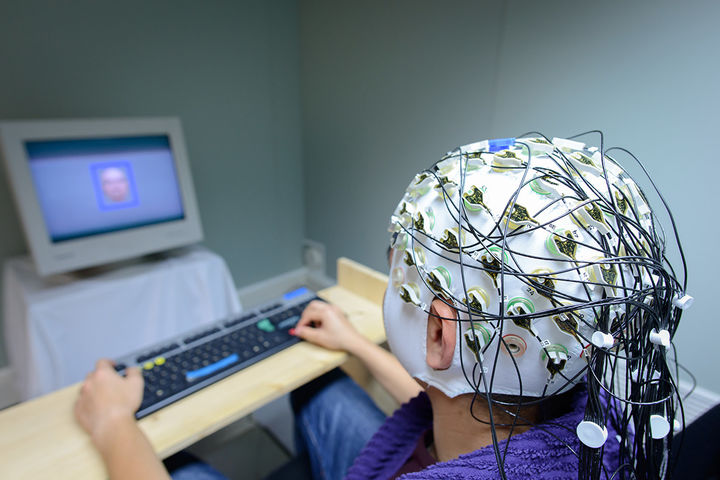 A person is wearing a clothing to measure mind waves and is looking at a computer screen with a face on it.