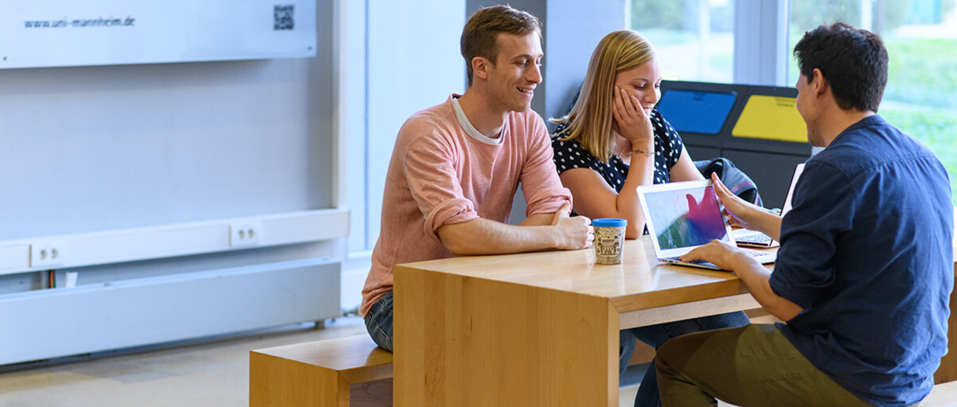 Drei Studenten sitzen an einem Tisch in der Universität und sprechen miteinander.
