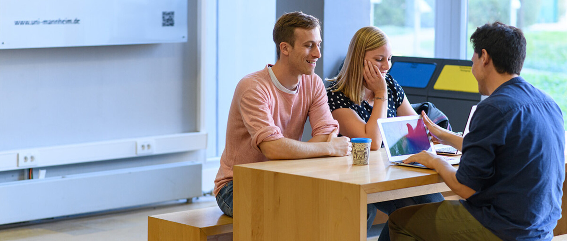 Drei Studenten sitzen an einem Tisch in der Universität und sprechen miteinander.