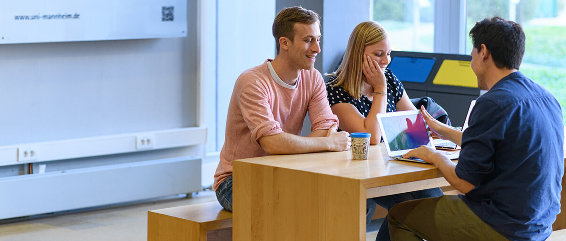 Drei Studenten sitzen an einem Tisch in der Universität und sprechen miteinander.