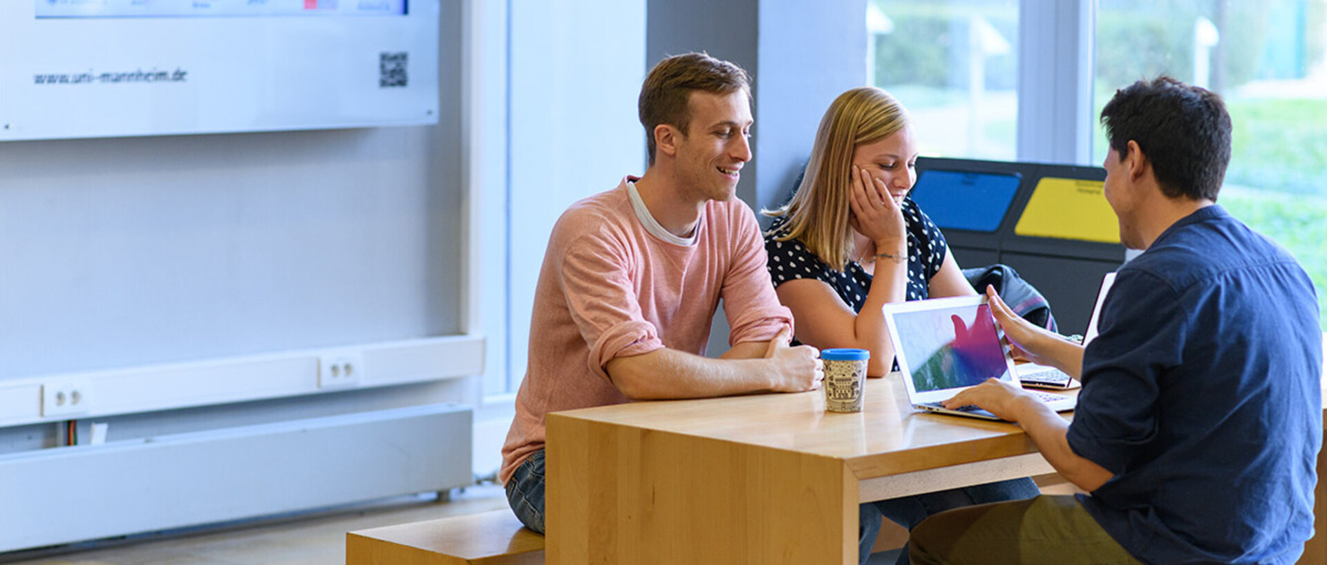 Drei Studenten sitzen an einem Tisch in der Universität und sprechen miteinander.