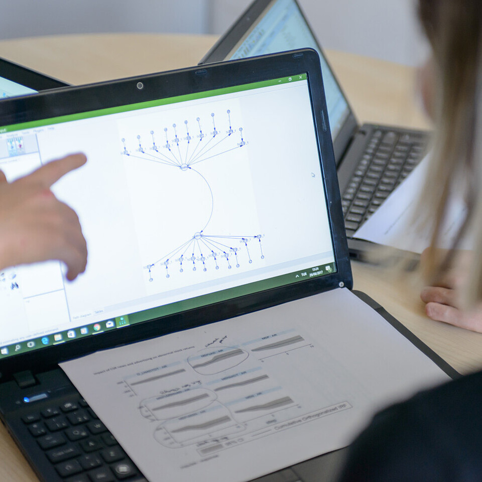 Ein aufgeklappter Laptop steht auf einem Tisch. Eine Person zeigt mit ihrem Finger auf die Grafik, die auf dem Laptop angezeigt wird.