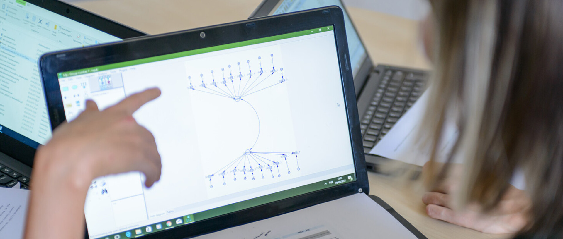 Ein aufgeklappter Laptop steht auf einem Tisch. Eine Person zeigt mit ihrem Finger auf die Grafik, die auf dem Laptop angezeigt wird.