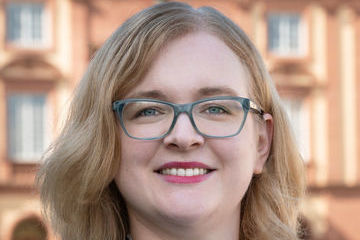 Prof. Rhese hat schulterlange blonde Haare und trägt eine Brille.