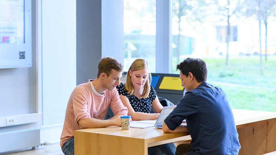 Drei Studierende sitzen an einem Tisch und lernen