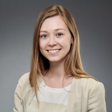 Polina Mosolova has her long blonde hair down. She is wearing a beige blazer and a beige and white striped shirt.