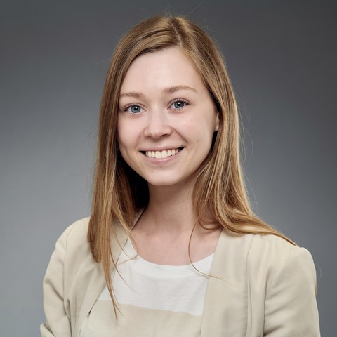 Polina Mosolova has her long blonde hair down. She is wearing a beige blazer and a beige and white striped shirt.