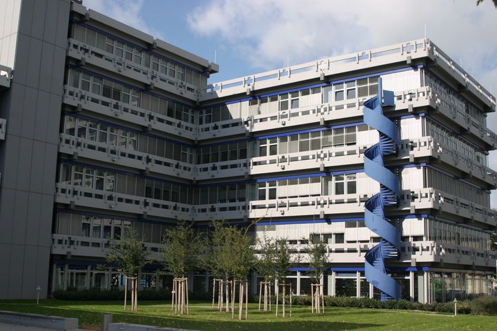 Gebäude der Fakultät für Sozial­wissenschaften mit blauer Wendeltreppe. Davor eine Wiese mit Bäumen.