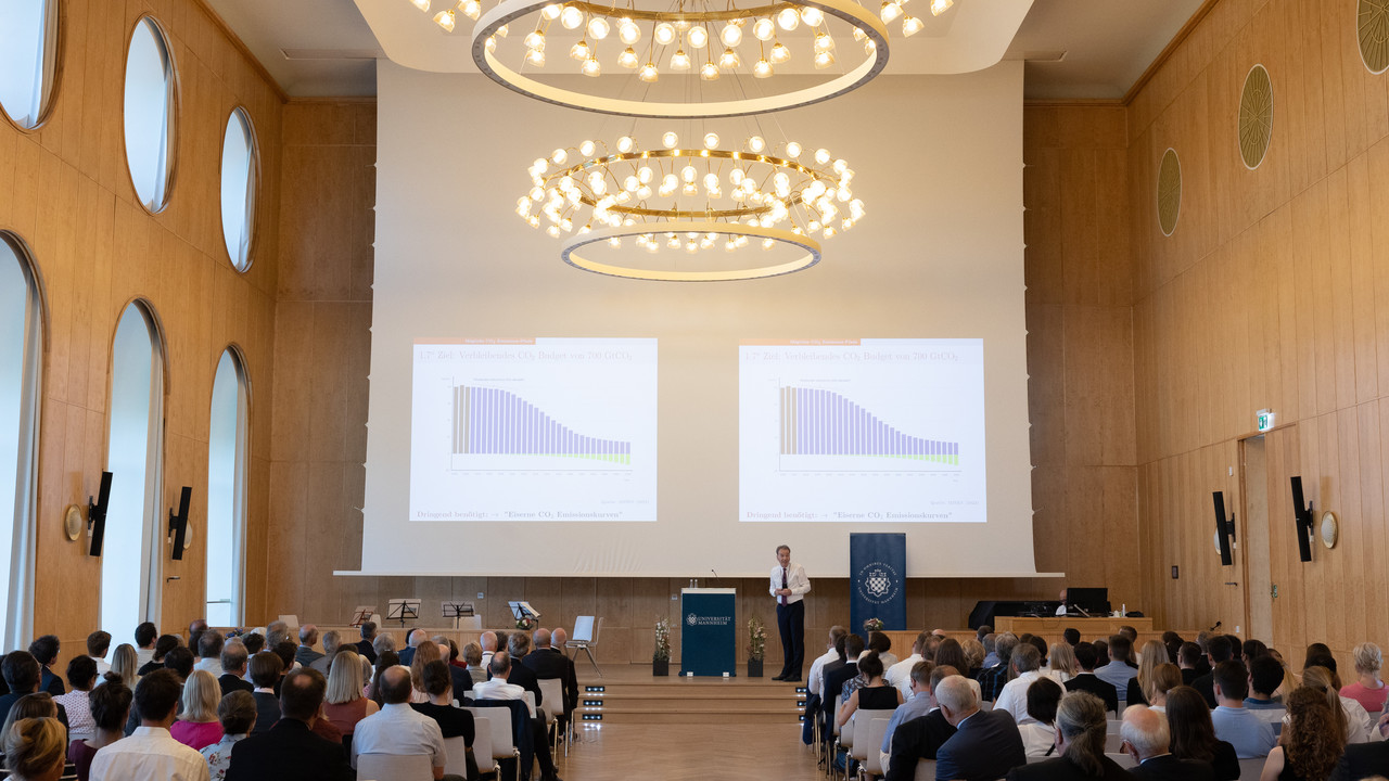 Vortrag in voll besetzter Aula der Uni Mannheim. Leuchtende Kronleuchter an der Decke.