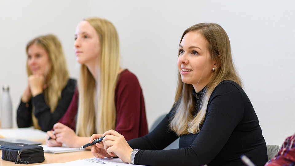 Drei Studentinnen sitzen nebeneinander in einem Seminarraum.