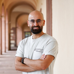 Hassan Abdolaziz stands smiling in an entrance hall of the Schloss. He wears a beige T-shirt and crosses his arms in front of his chest.