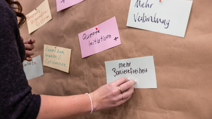 Jemand steckt eine Karte zu Wünschen für die UMA an eine Metaplanwand. Die Inschrift auf der Karte "mehr Barrierefreiheit"