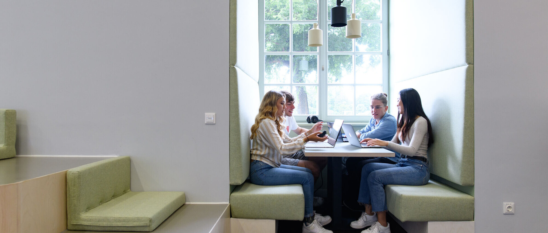Vier Studierende sitzen als Lerngruppe in einer Sitzecke mit Tisch in der Bibliothek.