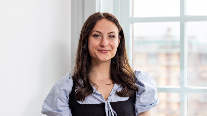 Giuliana Francesca Manganaro hat lange braune Haare. Sie trägt eine helle Kurzarmbluse und ein schwarzes Oberteil darüber.