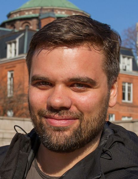 Portraitfoto. Im Hintergrund sind Häuser zu sehen.